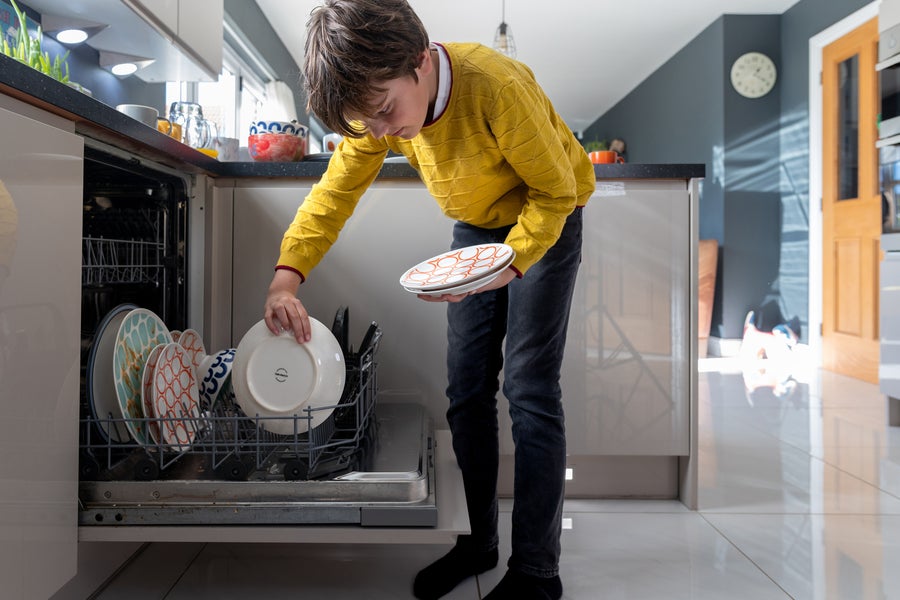 Young boy placing dishes into a dishwasher wearing a vibrant yellow jumper.