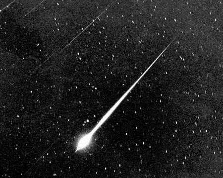 Streaks of light dart across a starry sky in black and white