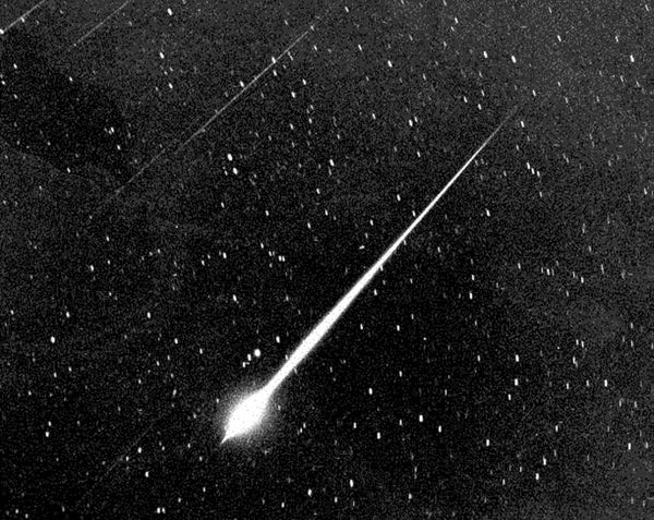 Streaks of light dart across a starry sky in black and white