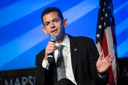 A man holds a microphone in front of a blue screen.