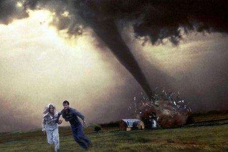 Two people run from a tornado directly behind them