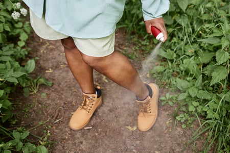 High angle closeup of Black woman spaying legs with bug repellent