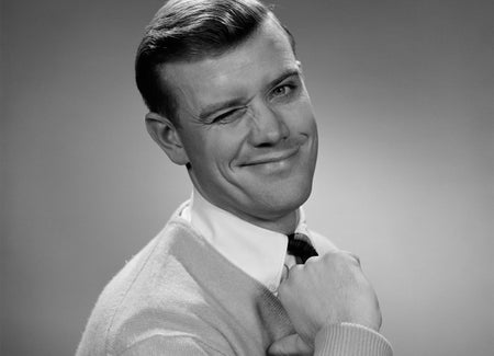 1950s smiling young man winking right eye and pointing proudly to himself.