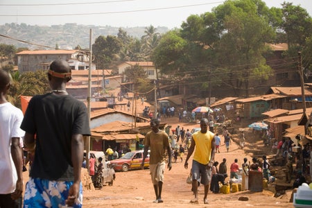 Young people walking on a dusty street with trees in background.