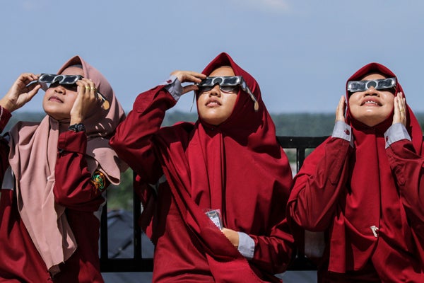 Three women wearing eye protective glasses looking up at the sun.