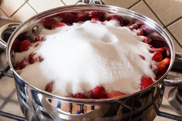 Making strawberry jam at home - heap of erythritol on fruit in stainless steel pot