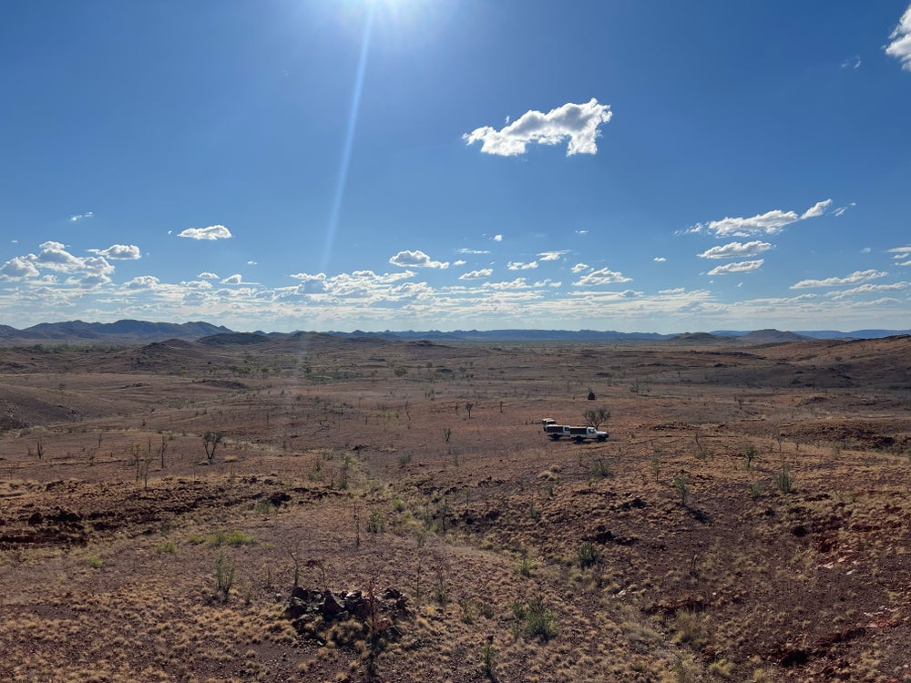 Un vehículo que conduce a través del paisaje de Pilbara con nubes blancas en cielos azules.