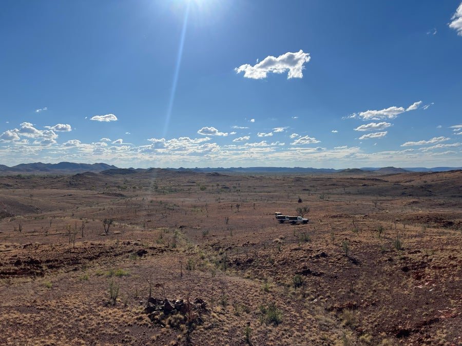 A vehicle driving through the Pilbara landscape with white clouds in blue skies.