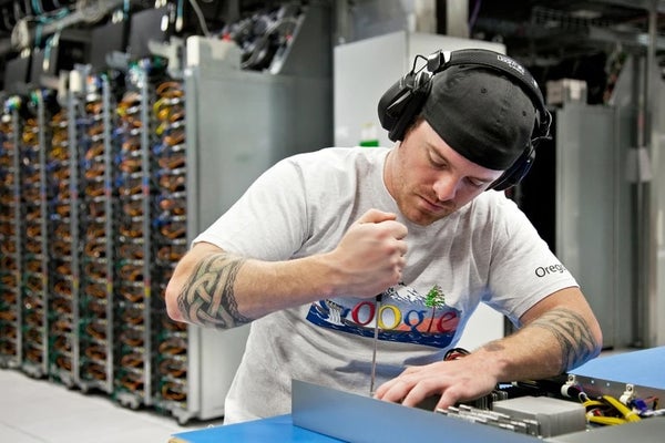 A man wearing a Google shirt, mending a technological device.