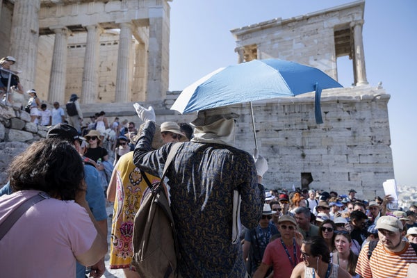 A tour group at the Acropolis led by a tour guide shielding himself from the sun with a light blue umbrella and white scarf and gloves