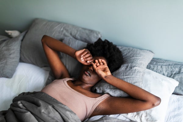 Woman rubbing eyes in bed struggling to wake up