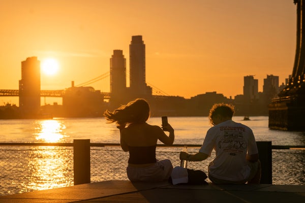 A couple sit on a park bench in Manhattan overlooking the East river while the sun rises during a heat wave