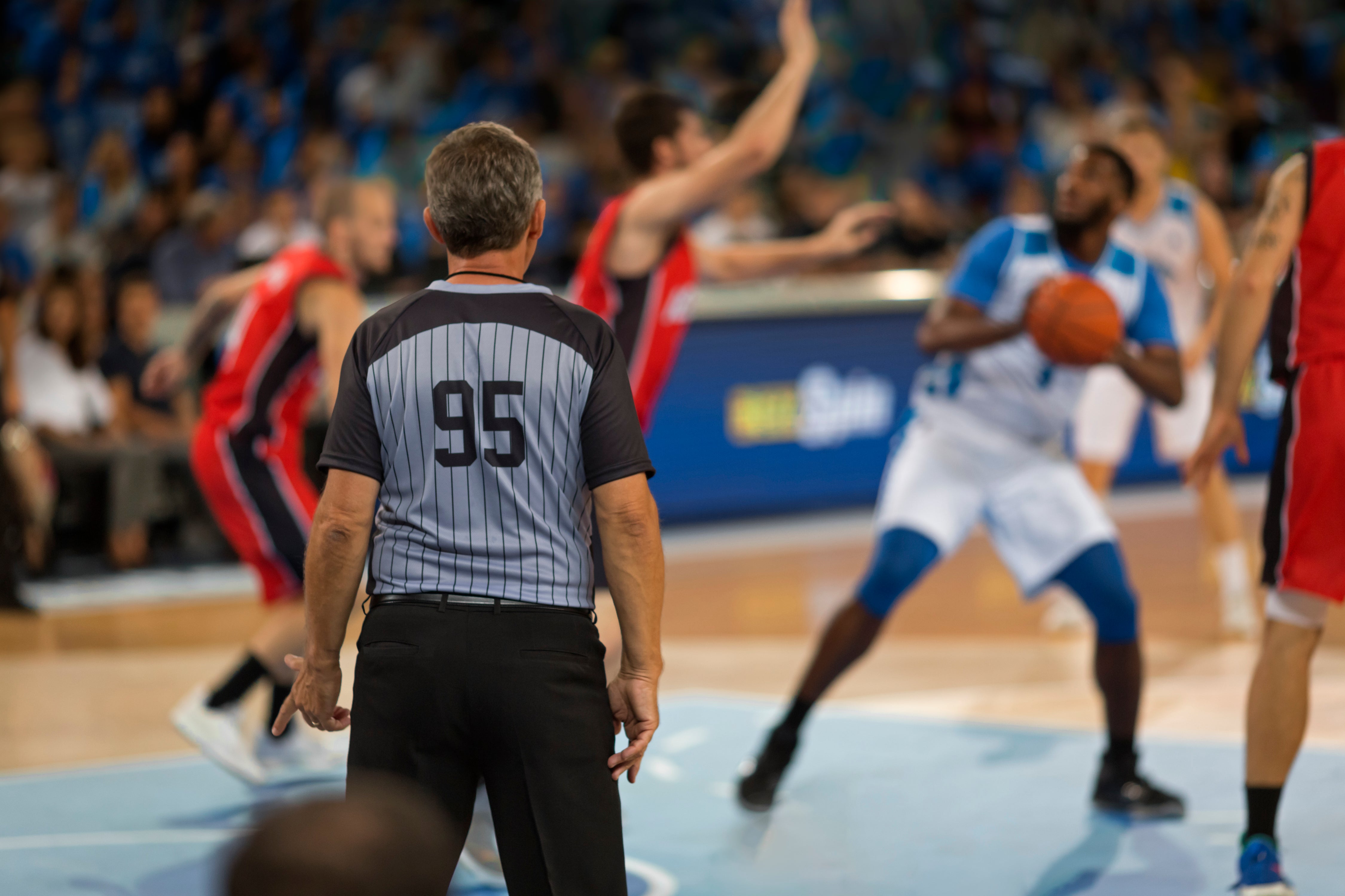 Referee in foreground monitors a basketball game, players seen in background