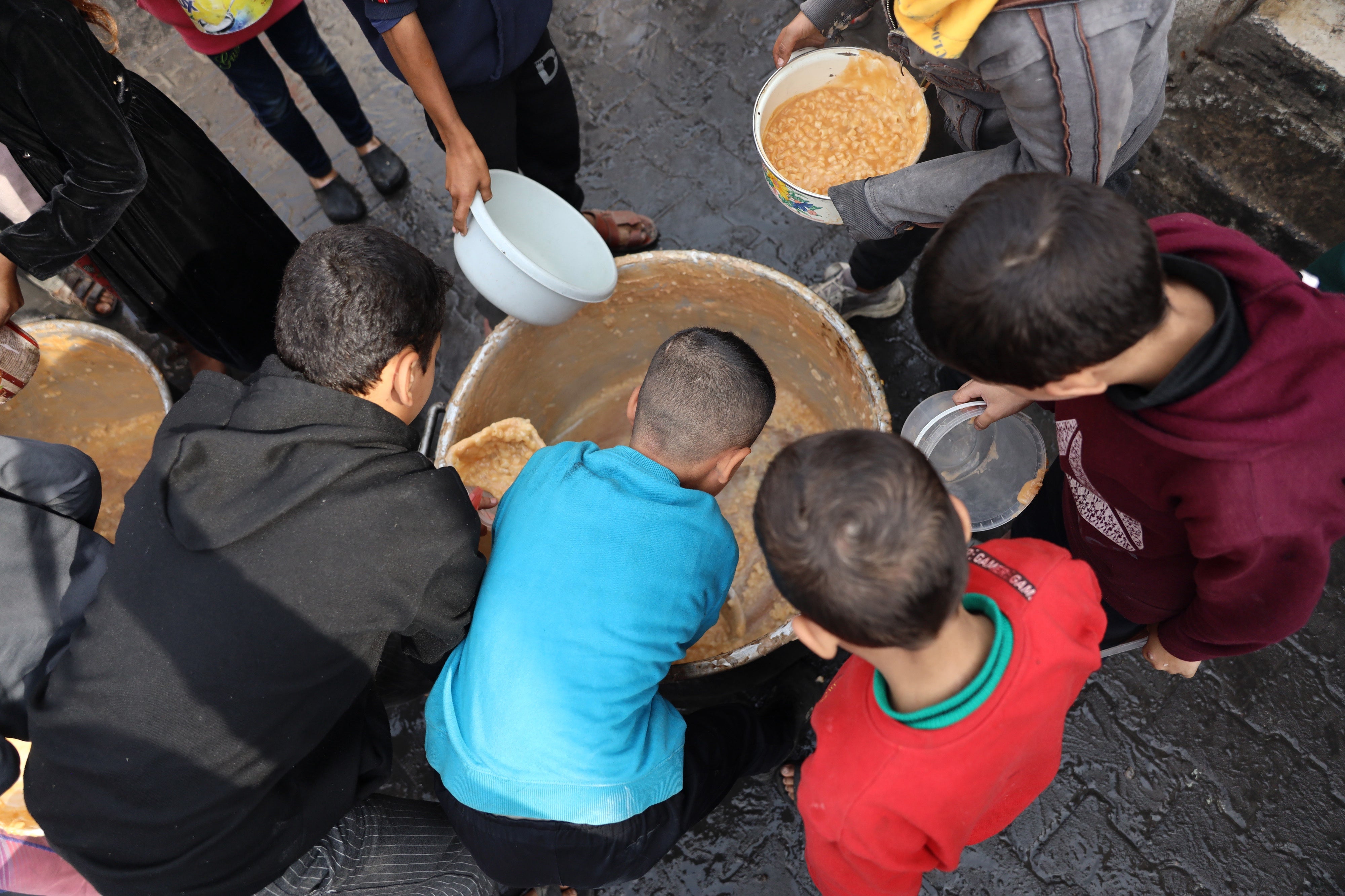 Backview of four young boys with black, blue and red shirts reaching into food containers.
