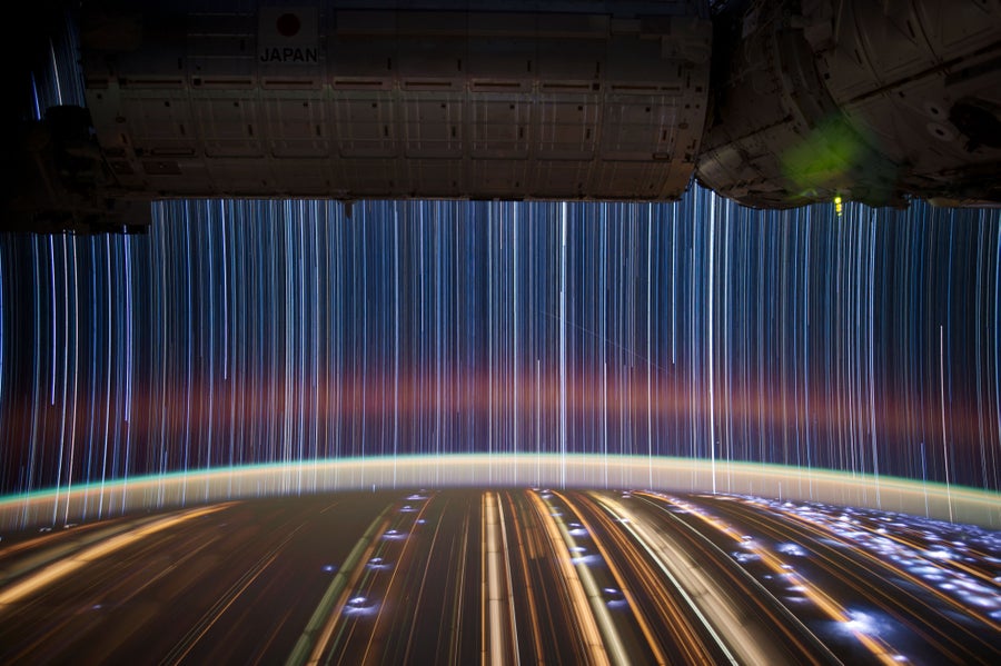Star trail composite image showing light trails from both stars in space and from city lights on earth made with photographs taken from inside the International Space Station