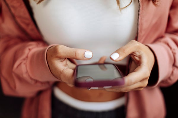 Young woman in dark pink jacket using smartphone with both hands