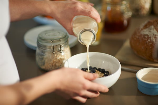 close up of a person's hands pouring milk from a bottle into a bowl of oats and blueberries