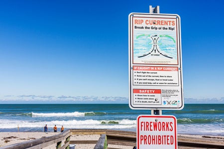 A sign at the entrance path at a Florida beach warns and provides safety tips to visitors about rip currents