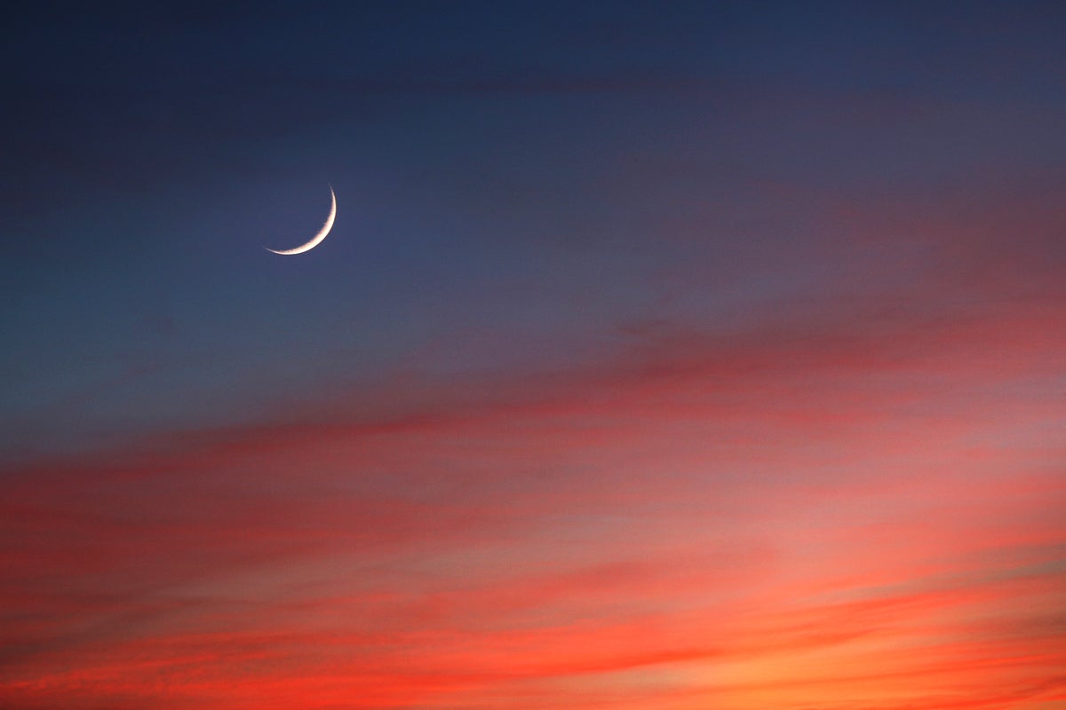 A crescent moon at twilight, against a colorful sunset