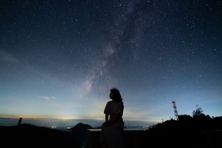 A silhouetted figure sitting on a bench beneath a dark starry sky