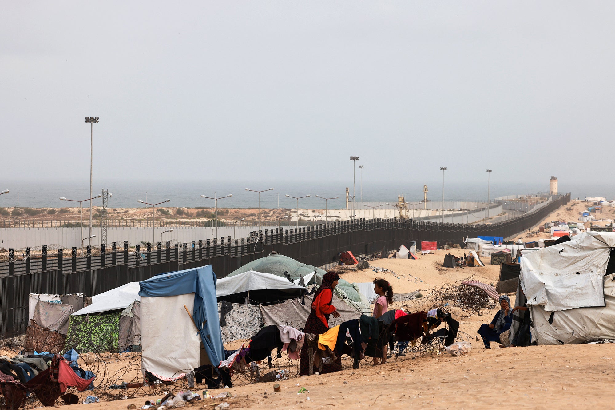 Displaced Palestinians standing outside their tents along a security fence along the border between Gaza Strip and Egypt