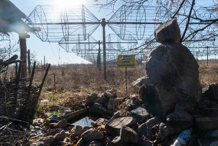 Boulders and trash are piled in the foreground of a large array of radio antennas beneath a sunny blue sky.