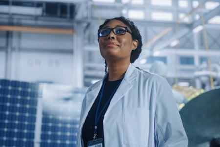 Black female engineer looking up and smiling inside aerospace satellite manufacturing facility