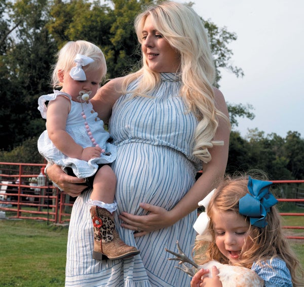 A woman holding a baby on her hip and a toddler standing below her, holding a chicken.