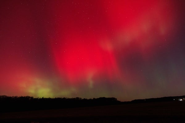 Red auroral lights cover the sky with a small bit of green right above the dark ground.