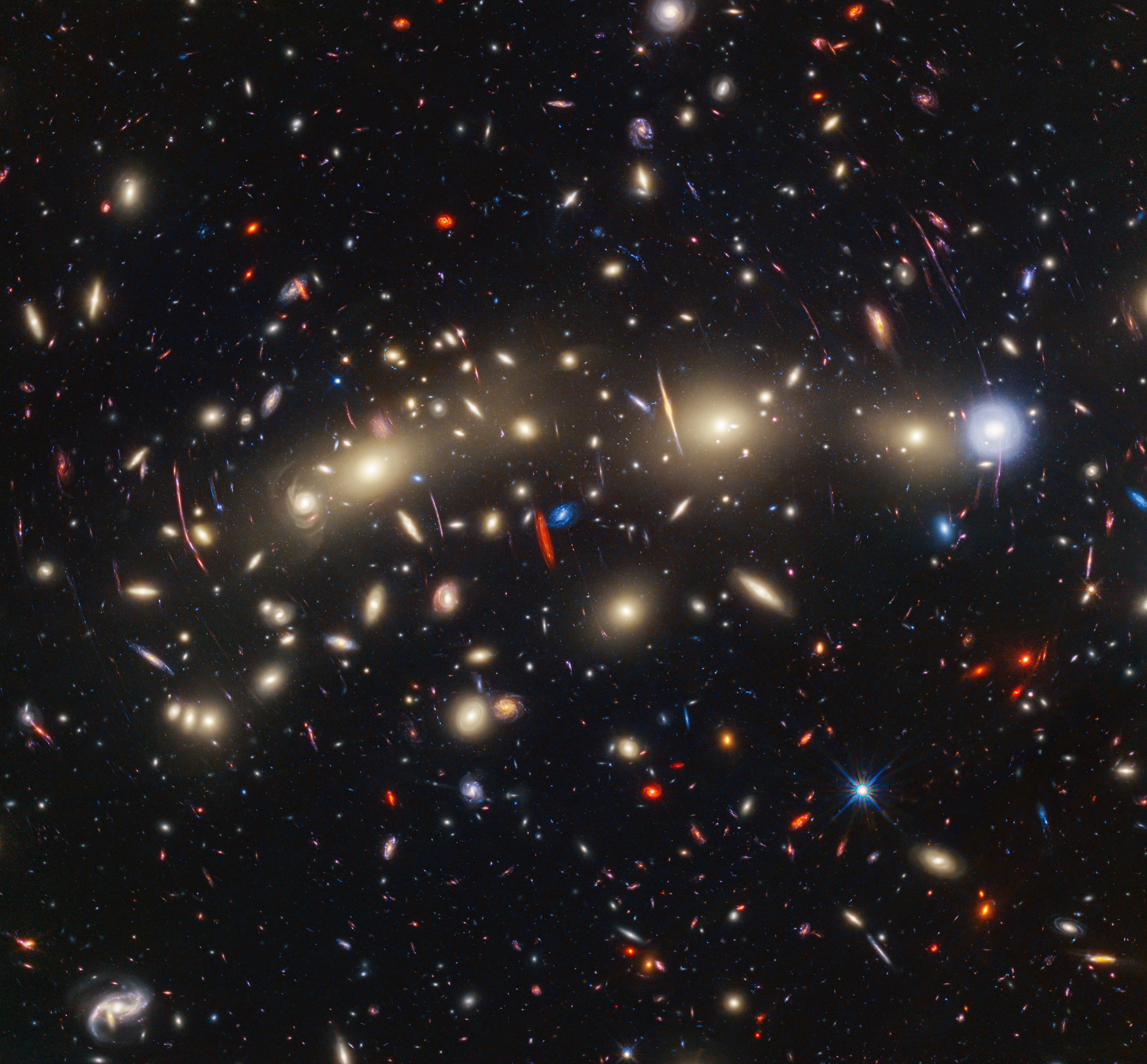 A full-color image of a large galaxy cluster. Some galaxies are warped by gravitational lensing.