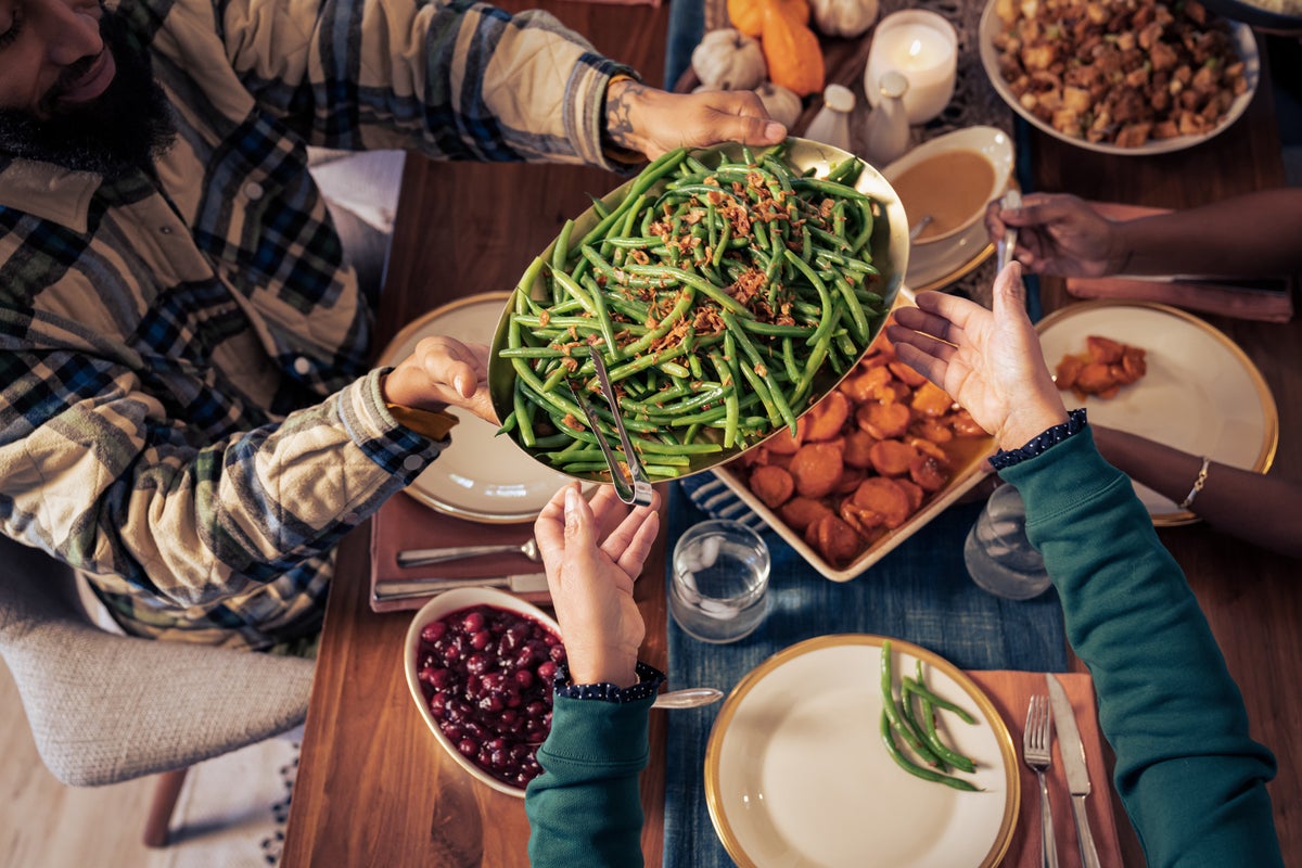 People gathered at a table for Thanksgiving dinner pass a platter of greenbeans