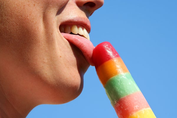 Close up of person licking a colorful ice pop with a blue sky background