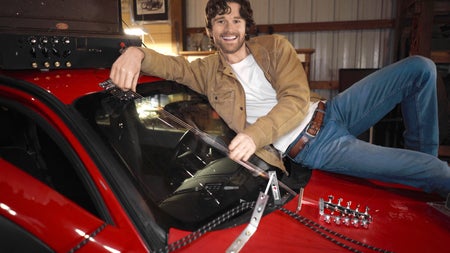 Jim Lill sitting on the hood and windshield of his car which he has modified into a functioning guitar