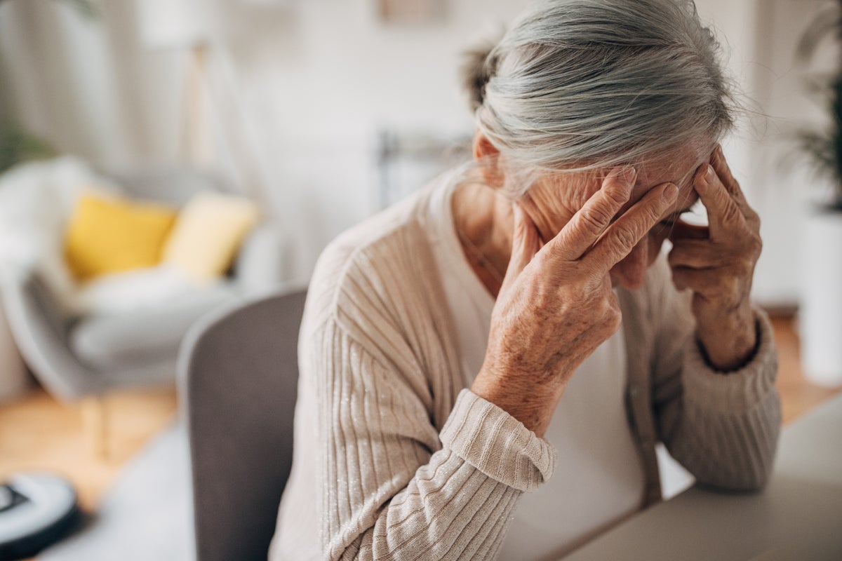 Old woman holding head in pain at home.