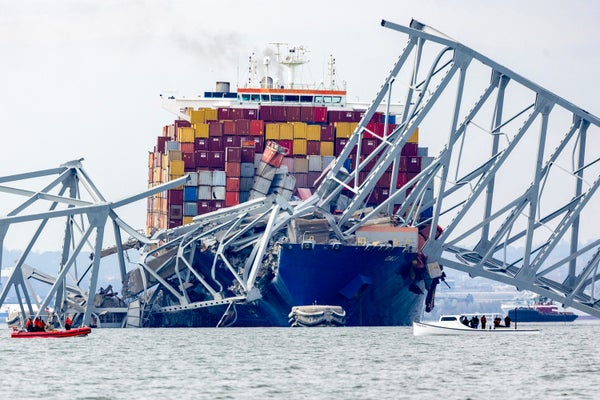 Cargo ship sits motionless behind collapsed and twisted metal bridge