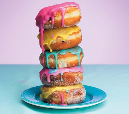 Five donuts stacked on a blue plate against a pink background