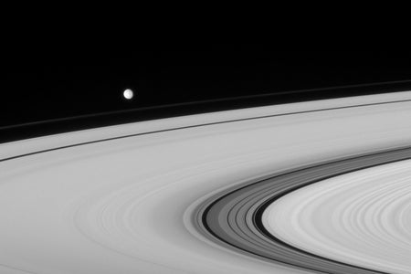 Saturn's moon Mimas circling rings of saturn.