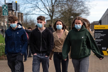 Students wearing face masks walk through the campus of the University of Kent in England after an outbreak of meningitis caused the deaths of two people