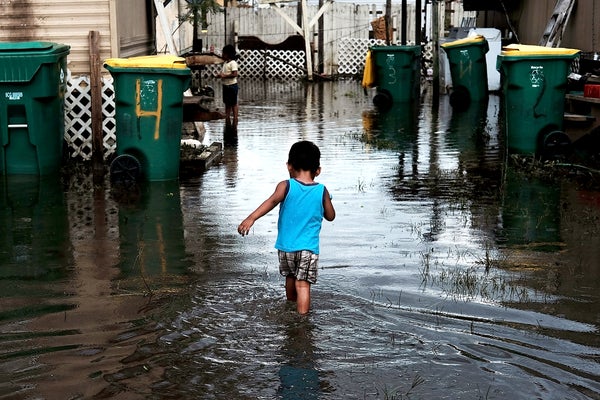 A child walks away from the camera on a flooded street.