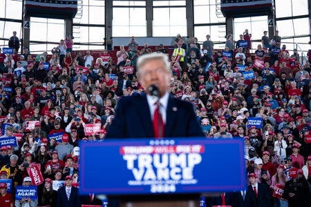 Attendees standing behind an out of focus Donald Trump at a campaign rally