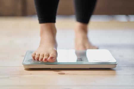 Female feet with red nail polish and black pants on scale.