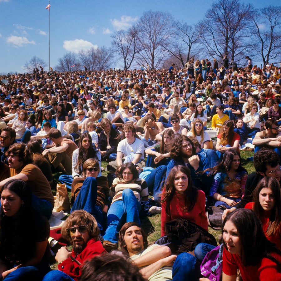 Huge 70's crowd sits on grass in park.