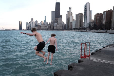 Two boys in black shorts jumping into Lake Michigan in front of the Chicago skyline