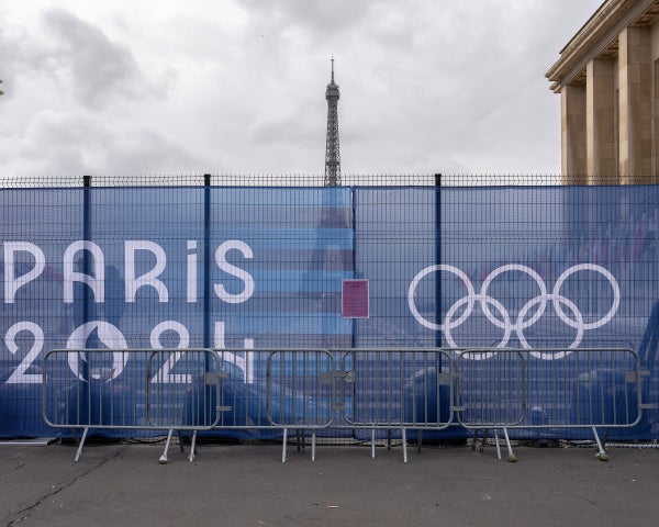 Barricades lined up in front of a logo of Paris 2024 and the Olympic rings printed onto fencing blocking off an area in Paris with the Eiffel Tower visible in the distance