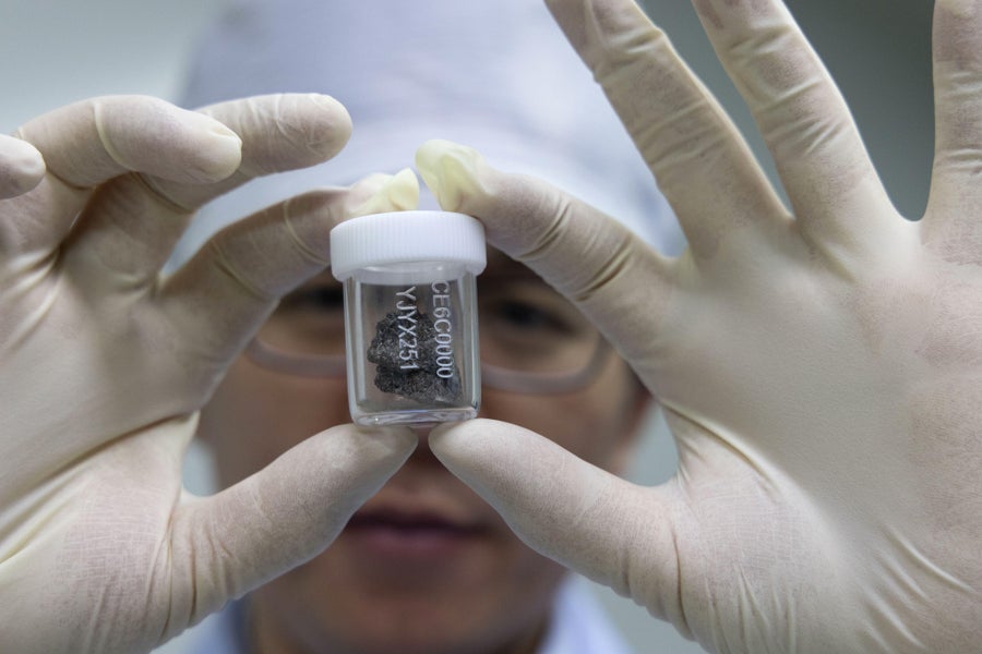 Researcher with white rubber gloves holding container w/ lunar sample.