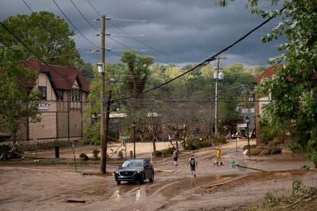 People walk down a street covered in mud and water to inspect the flood damage in the Biltmore Village in the aftermath of Hurricane Helene on September 28, 2024 in Asheville, North Carolina