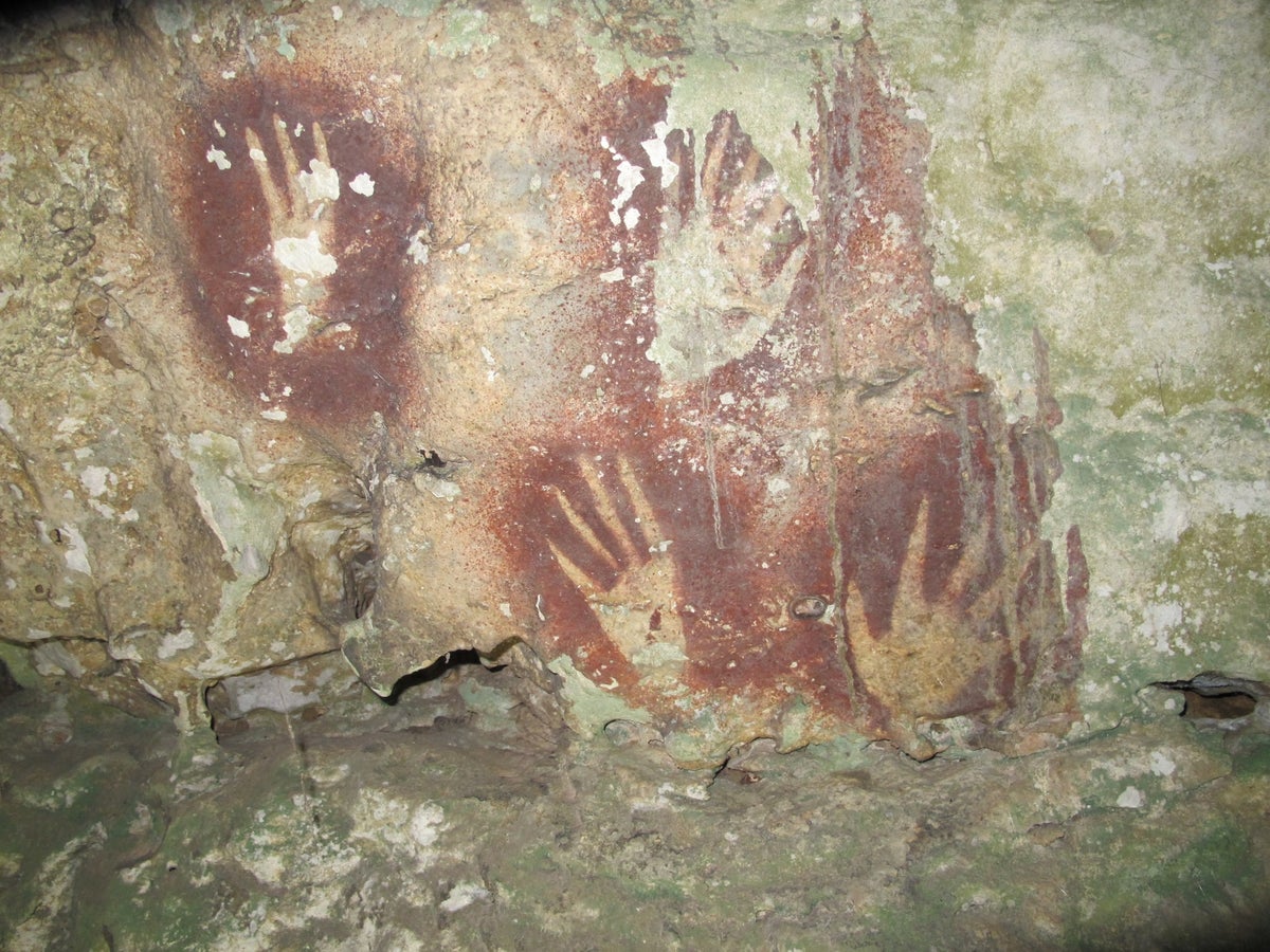 The outlines of hands in brown with narrowed finger tips on cave rock