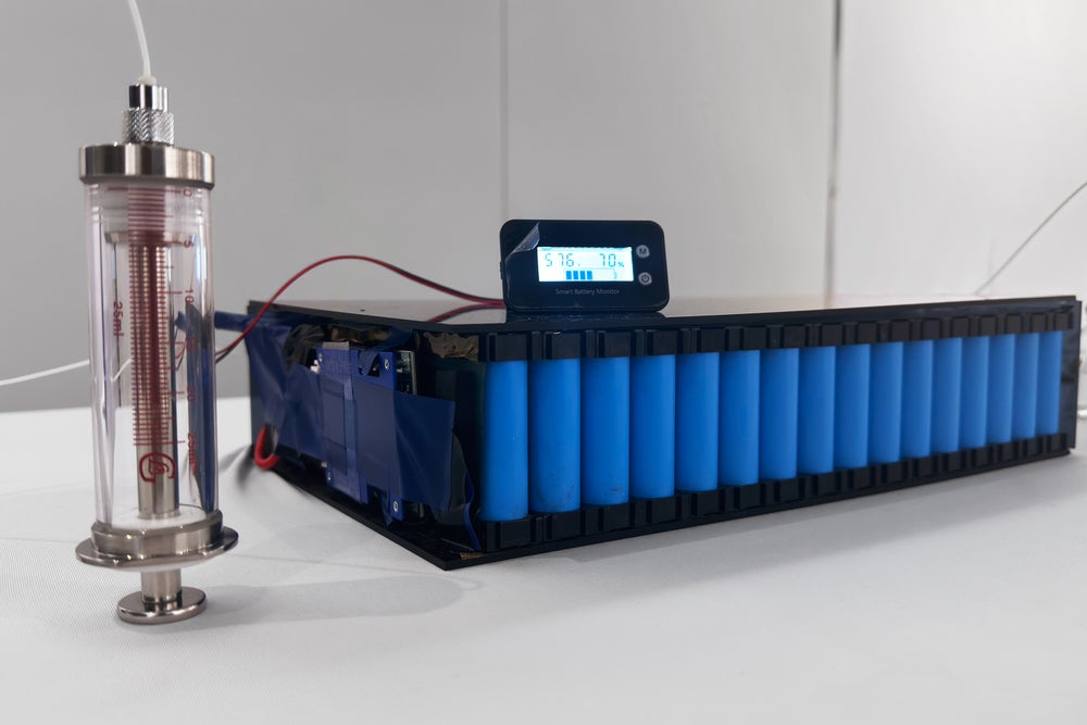 Configuración experimental que muestra el electrolito que se inyecta en un paquete de baterías azules gastadas en un banco de laboratorio blanco