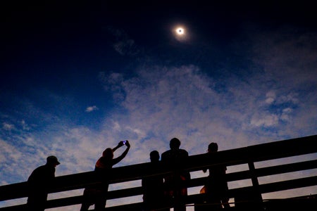 Person holding up cell phone to photograph solar eclipse as others around observe event