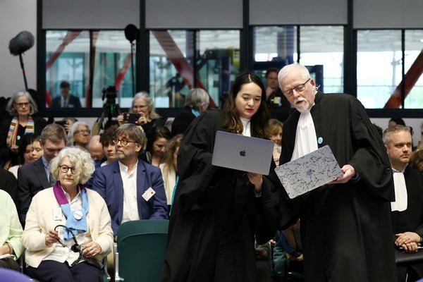 Courtroom with people and two representatives in black cloaks holding laptops.